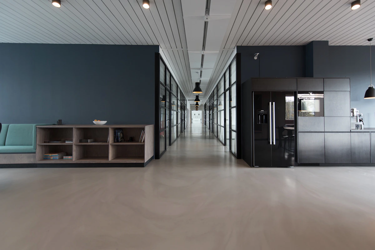 Empty modern office with a glass-walled corridor, a teal bench and a black kitchen unit