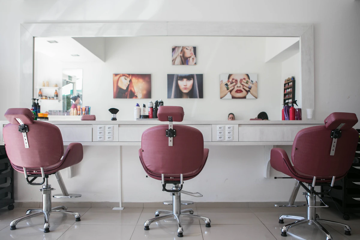 Empty hair salon with three burgundy styling chairs facing a long mirror