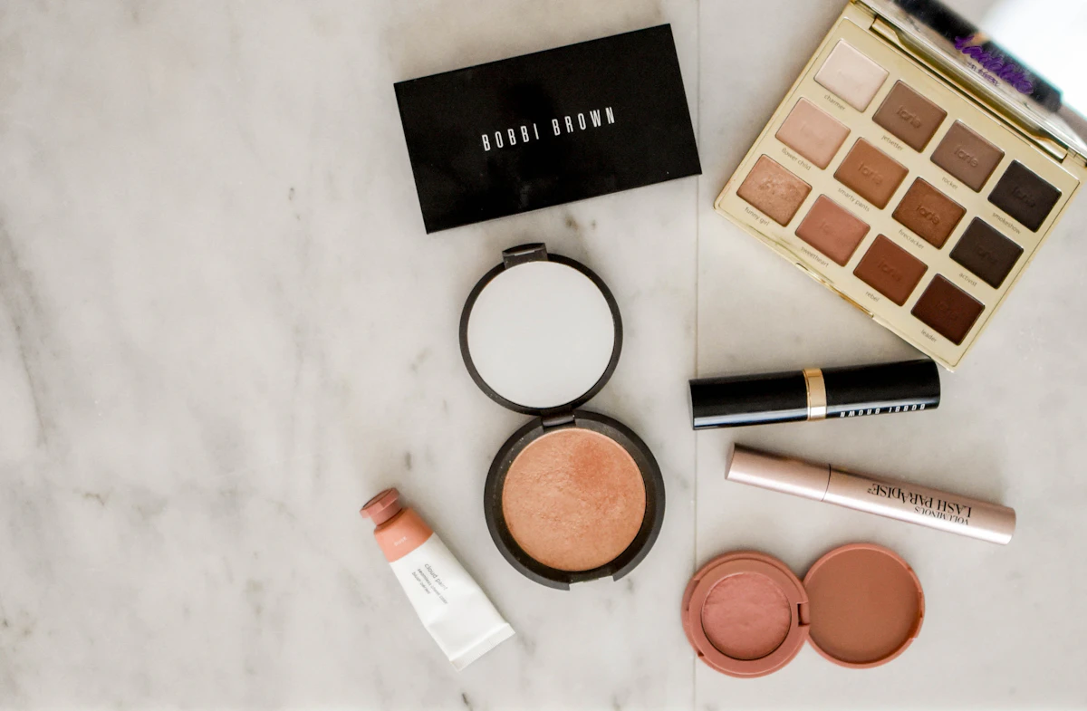 Makeup laid out on white marble: eyeshadow palette, bronzer, blush, lipstick and mascara