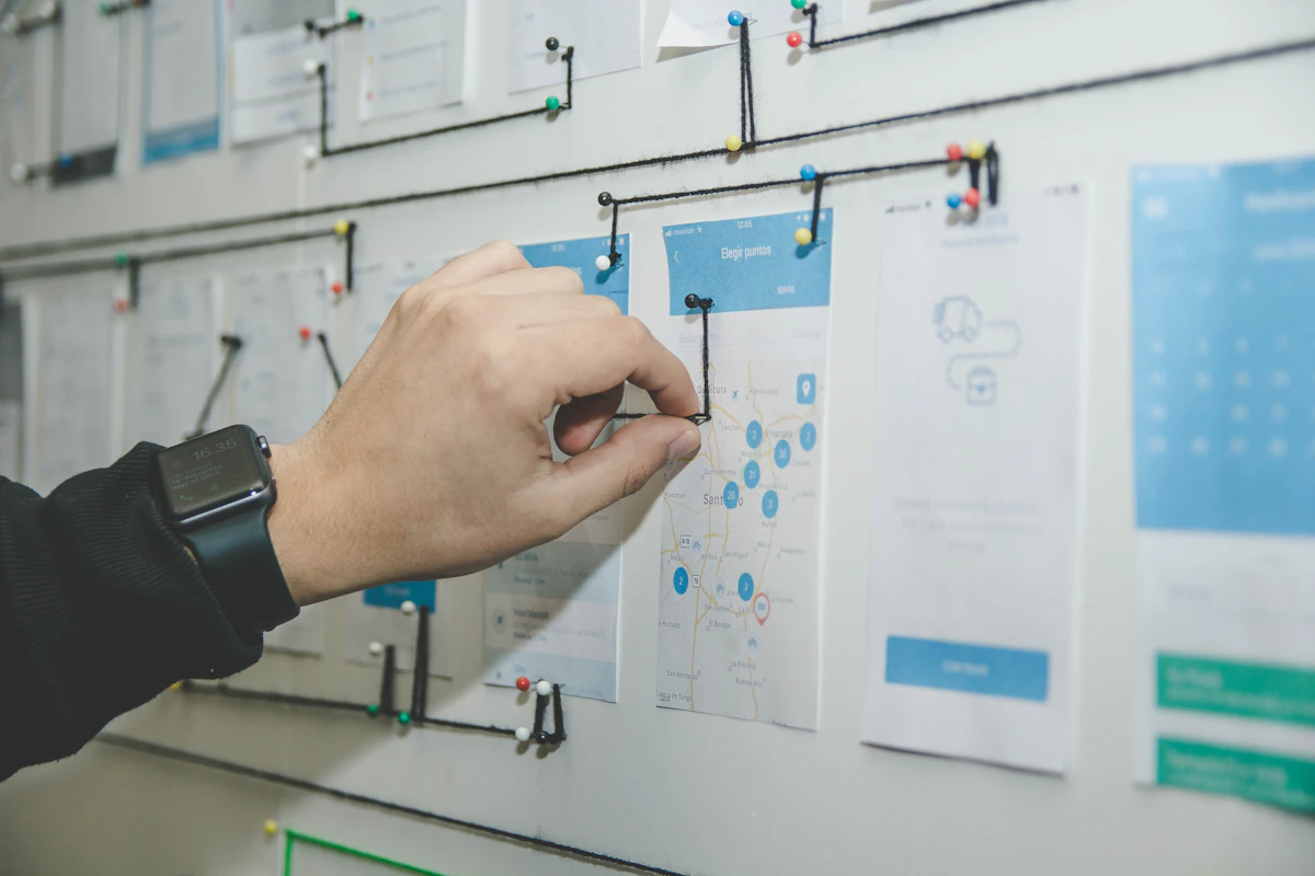 Hand pinning string between printed mobile app screens on a wall to map a user flow