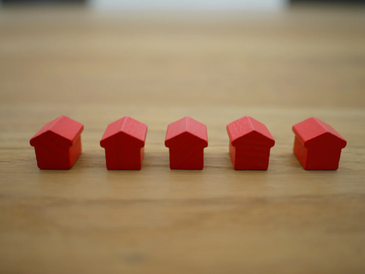 Five small red wooden house pieces in a row on a wooden table